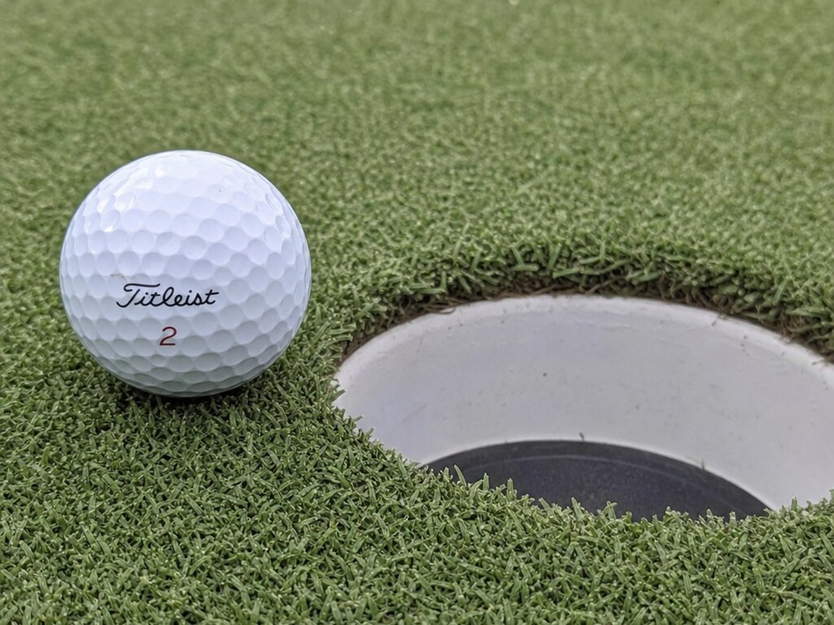 Titleist golf ball resting at the edge of the cup on premium synthetic putting green turf