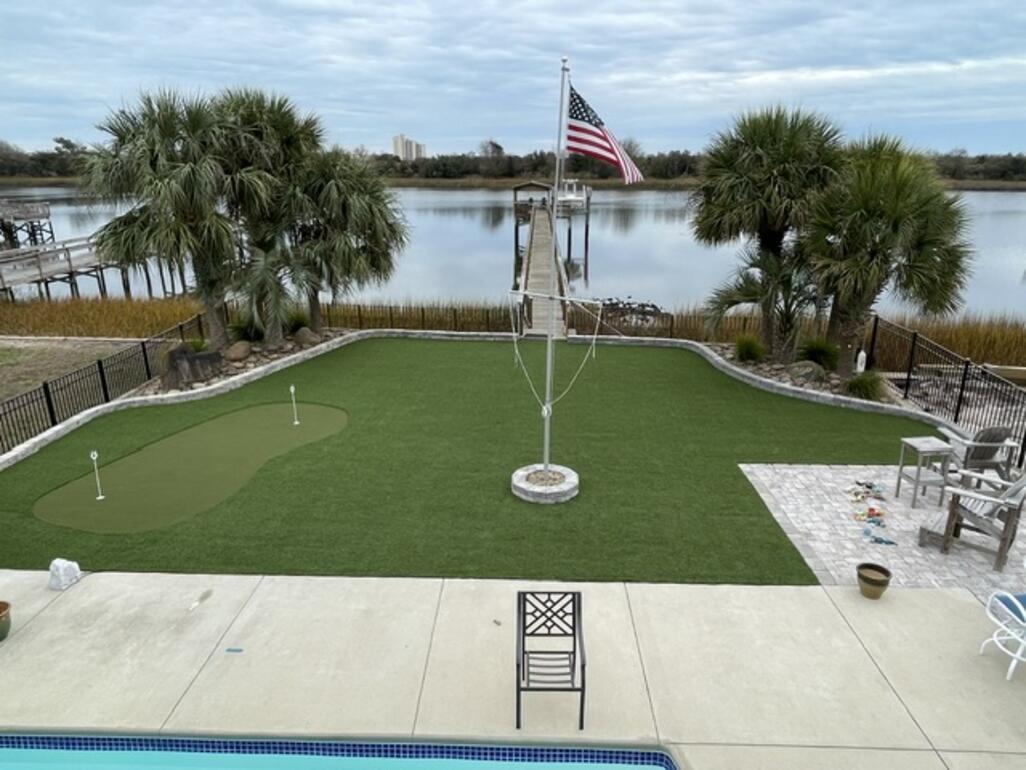 Backyard synthetic turf putting green and paver patio with an American flag, overlooking a tidal marsh at a Brunswick County home
