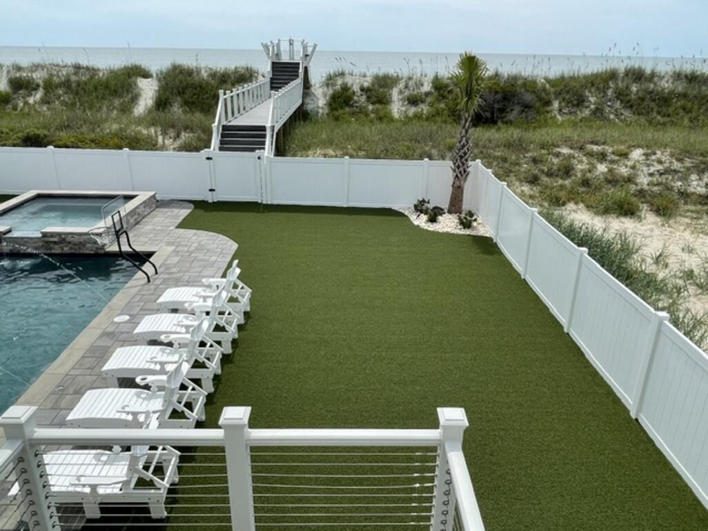 Oceanfront backyard with a manicured synthetic turf lawn beside a pool, steps from the beach dunes