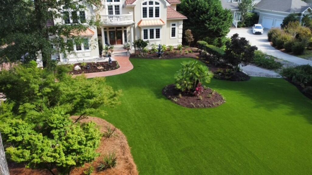 Drone view of a coastal estate front yard transformed with premium synthetic turf and curved planting beds