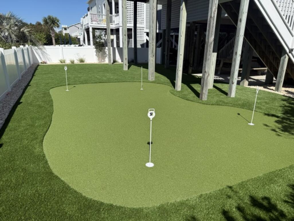 Multi-hole synthetic putting green installed in the shaded area beneath a raised coastal home