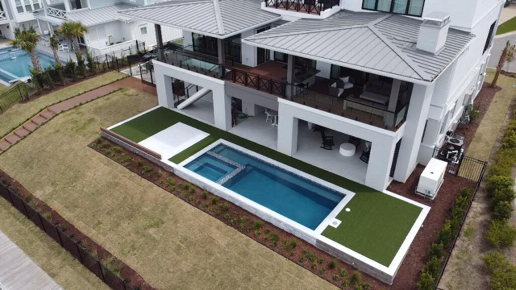 Aerial view of a modern beachfront home with synthetic turf surrounding a rectangular pool and spa