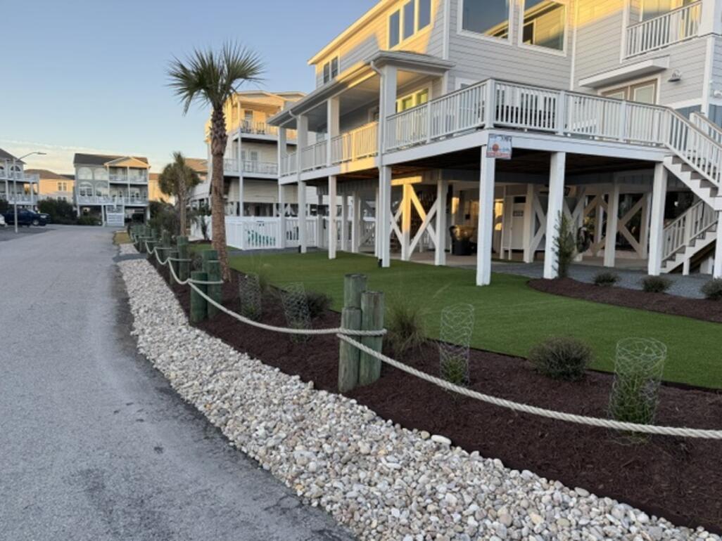 Coastal home curb appeal featuring a synthetic turf accent lawn, rope-and-post fencing, and white-rock ground cover
