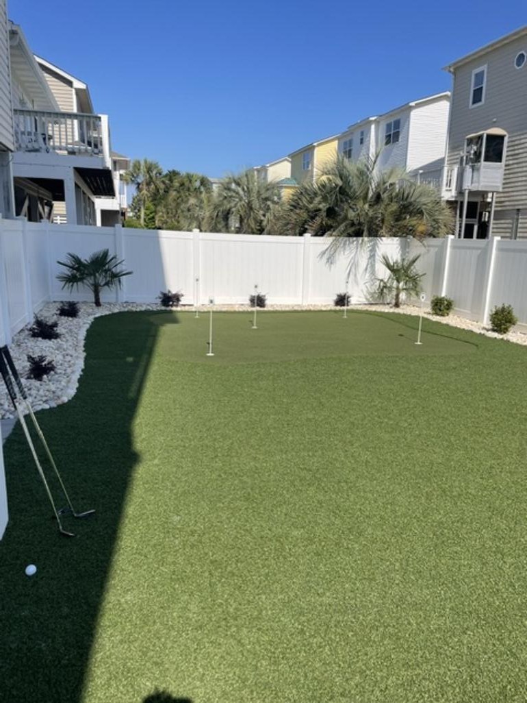Private backyard putting green with synthetic turf and golf clubs ready for practice under a clear blue sky