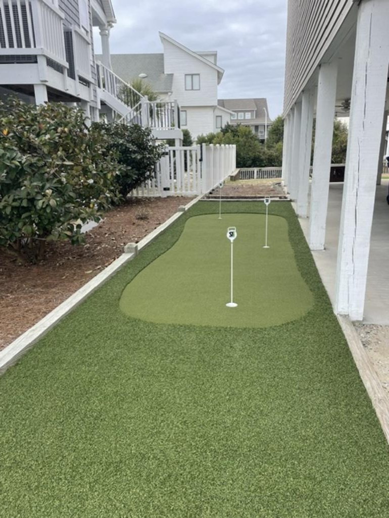 Narrow side yard transformed into a synthetic turf putting green beside a coastal home
